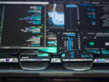 Glasses sitting on desk as data running through computers